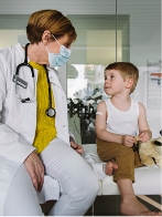 Medical professional wearing a mask and speaking to a young patient.