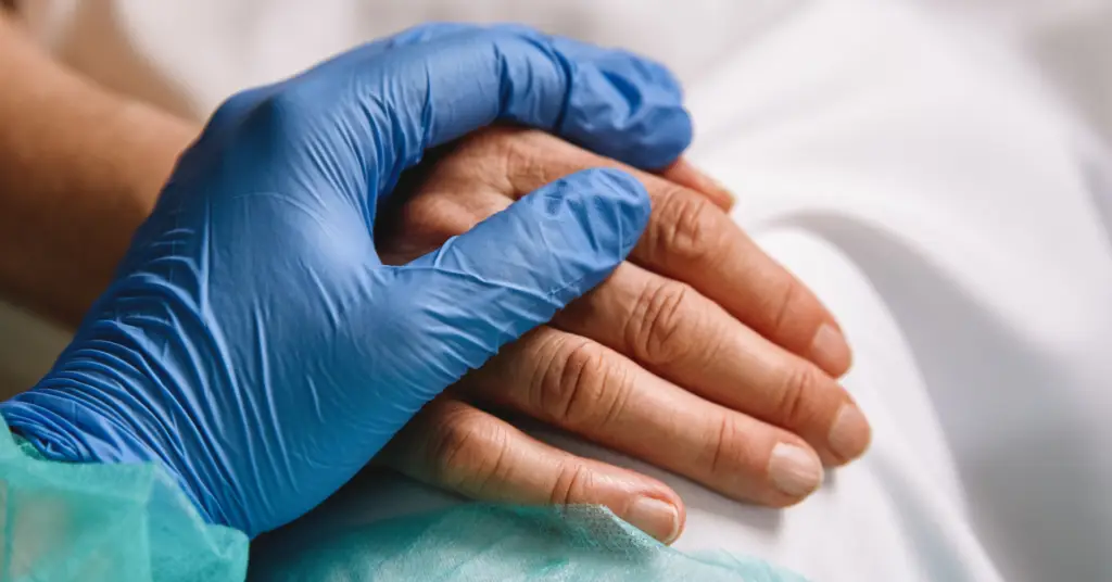gloved hand over a patient hand