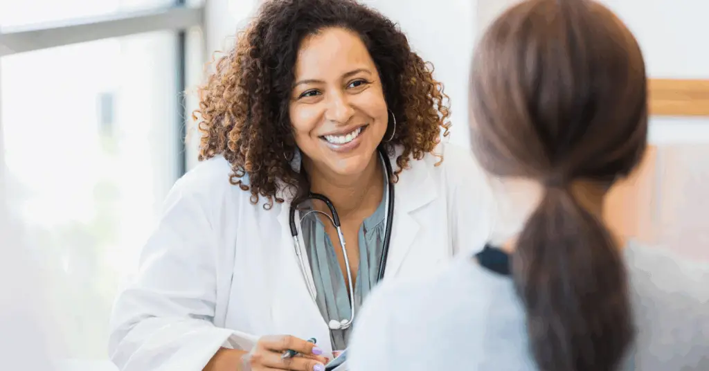A smiling mid adult female doctor listens as a female patient discusses her health