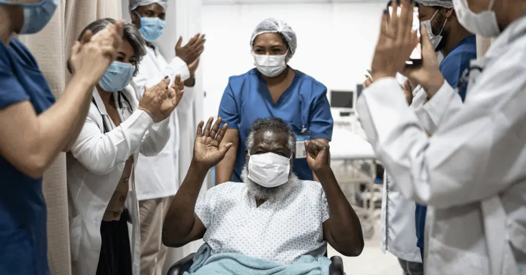 medical professional wheeling a covid patient through the hall cheering