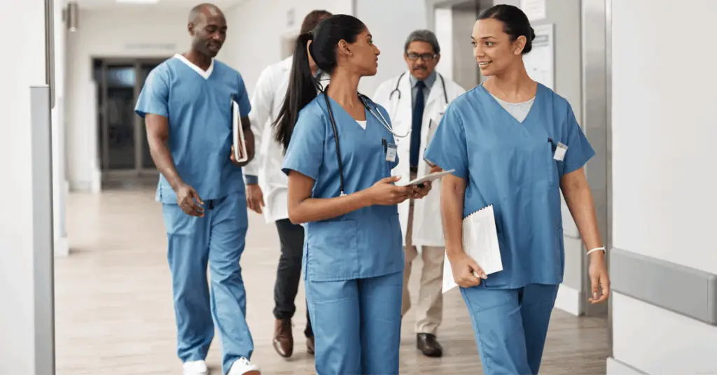 two nurses talking while walking through the halls with several doctors walking behind