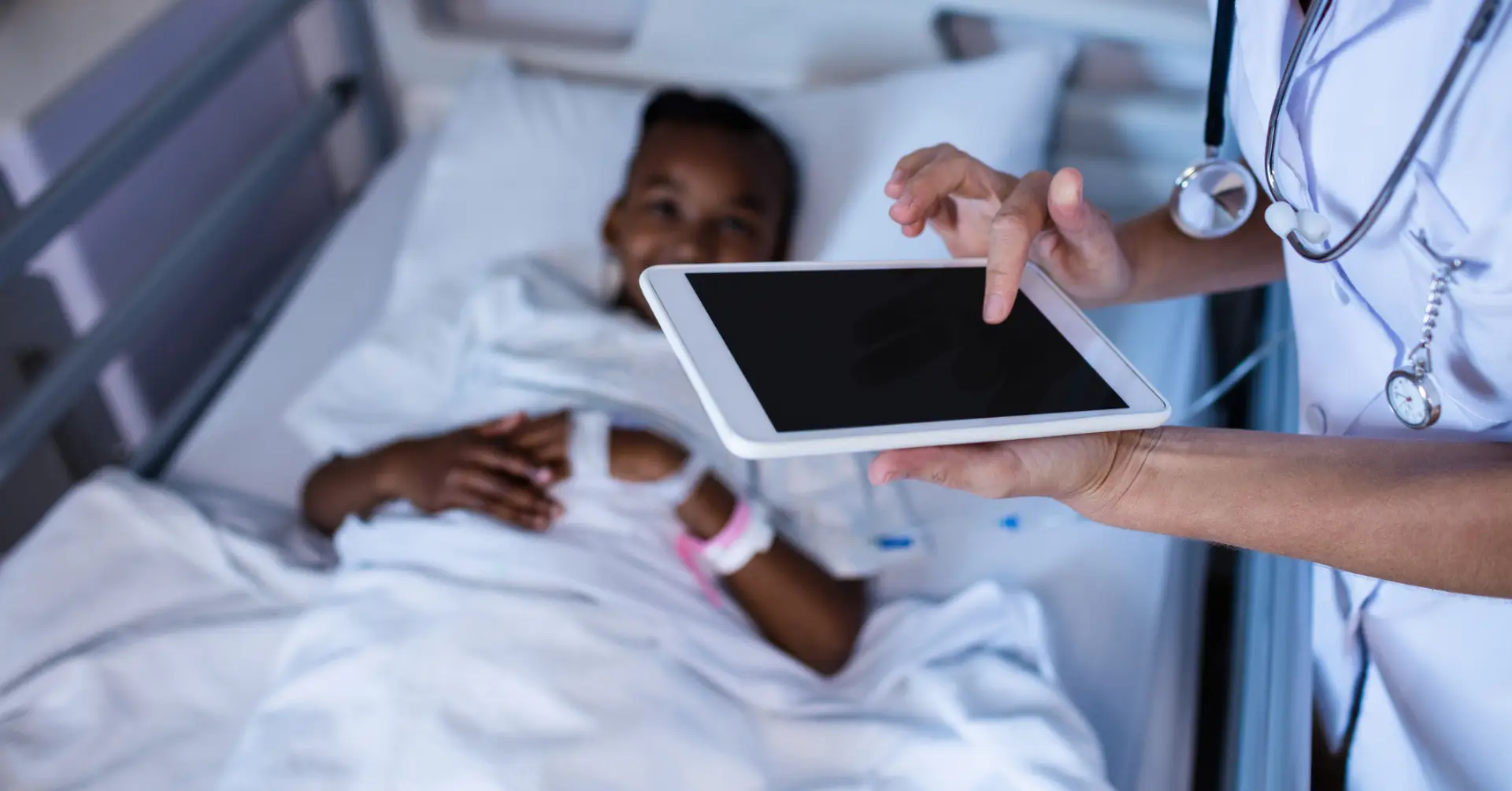doctor makes notes on tablet near patient in hospital bed