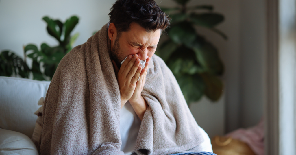 man sneezing wrapped in blanket sick