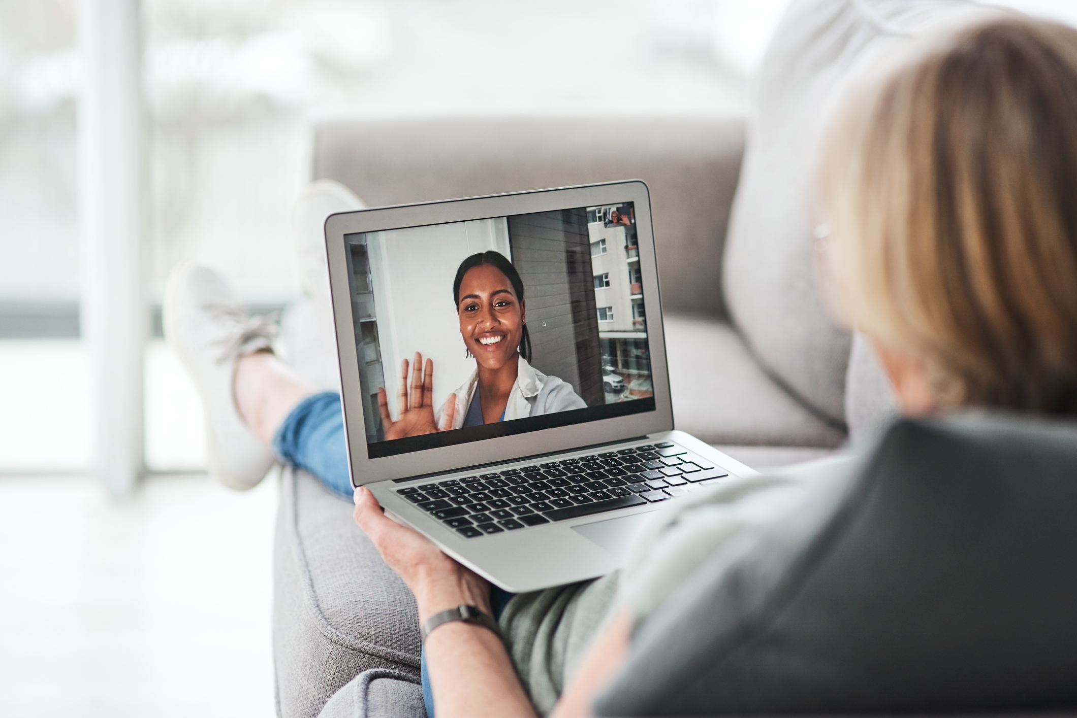 Medical professional waving at patient through a laptop during a telehealth appointment.