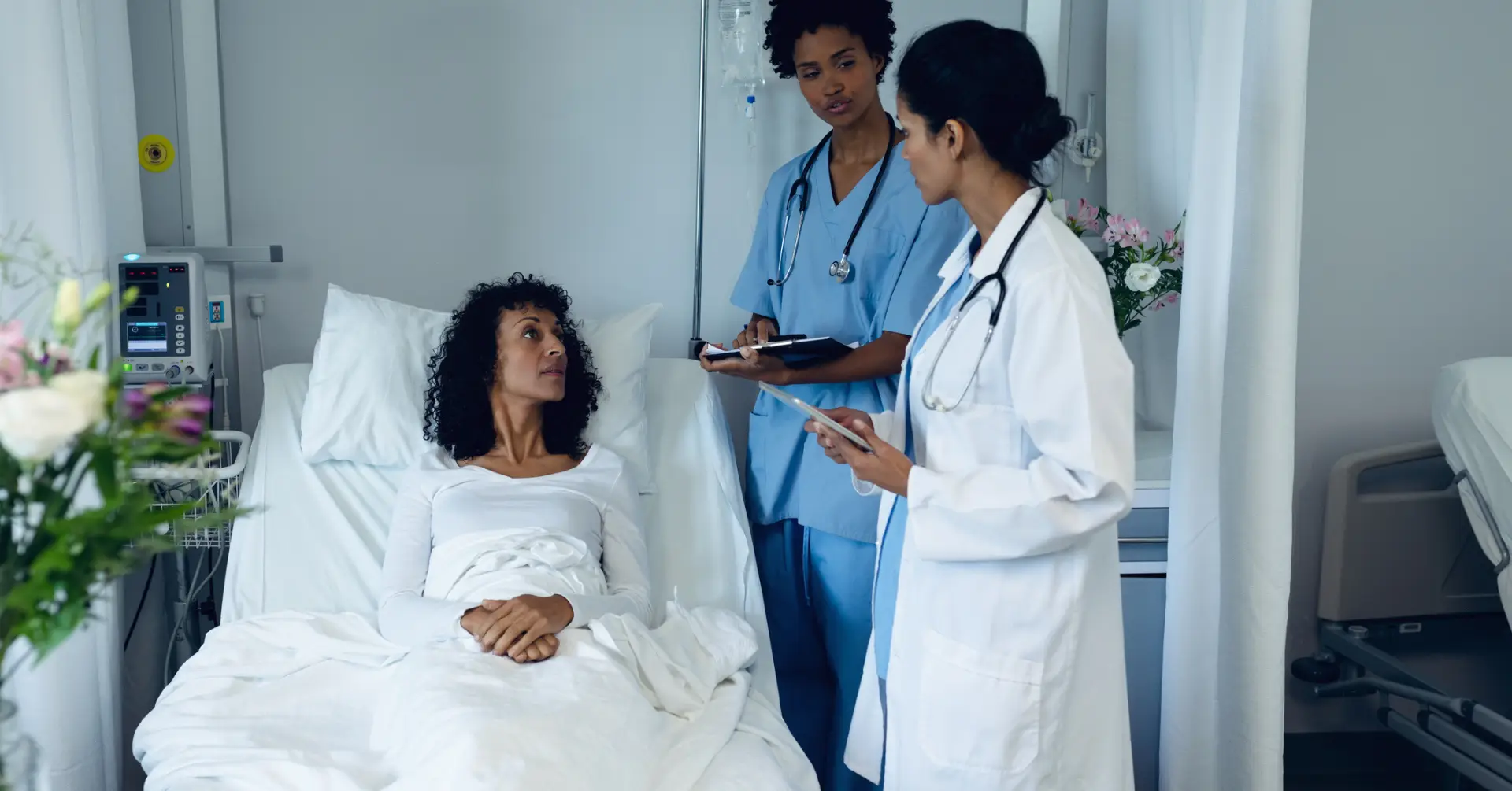 Side view of diverse female doctors interacting with mixed race female patient in the ward at hospital