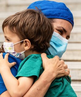 Medical professional wearing a mask hugs a young patient wearing a mask.