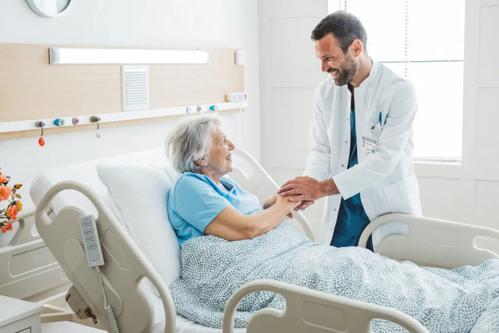 Doctor talking to senior woman in hospital bed. He is showing empathy for her condition