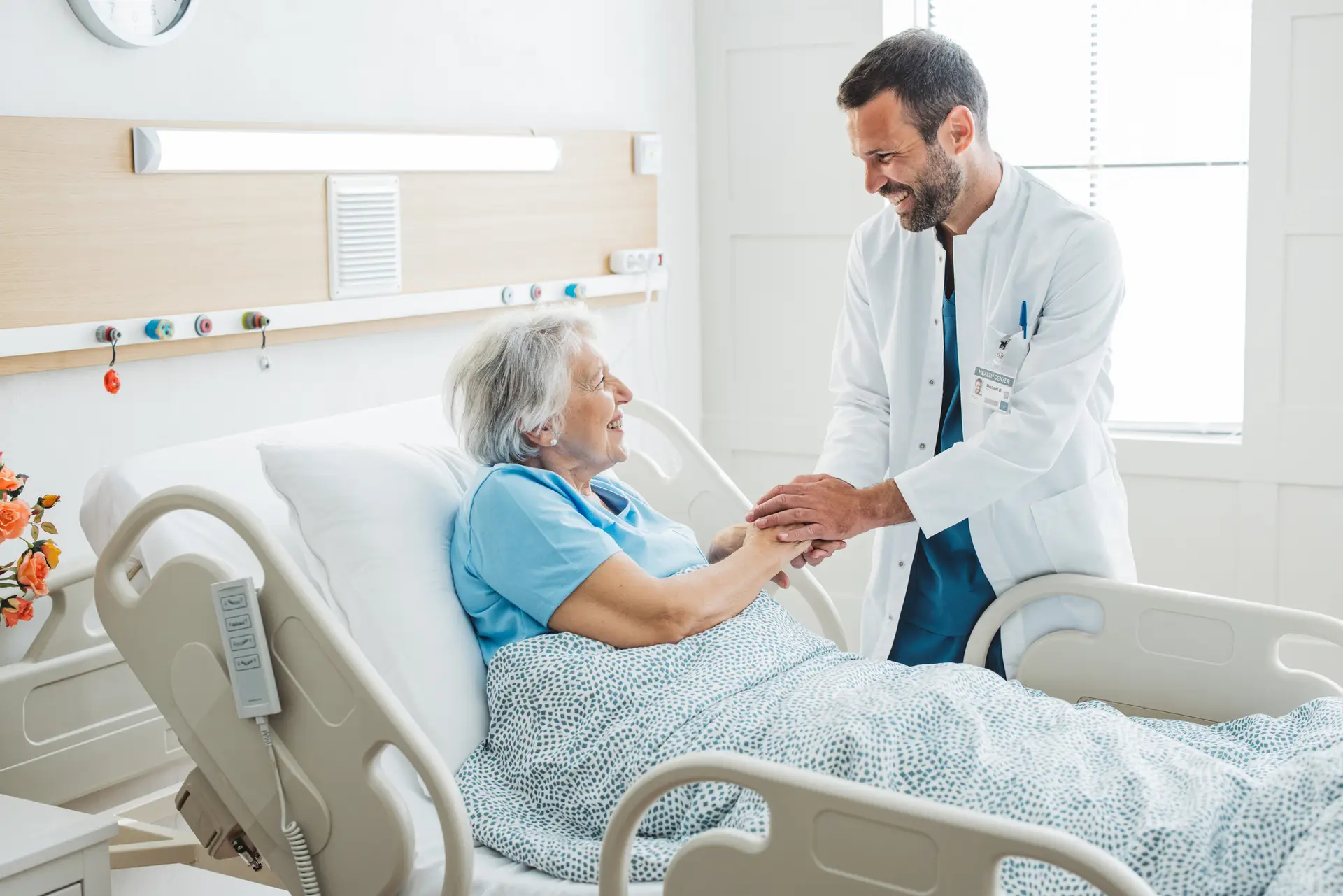 Doctor talking to senior woman in hospital bed. He is showing empathy for her condition