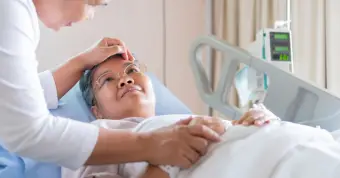 woman lying in hospital bed with someone holding her hand