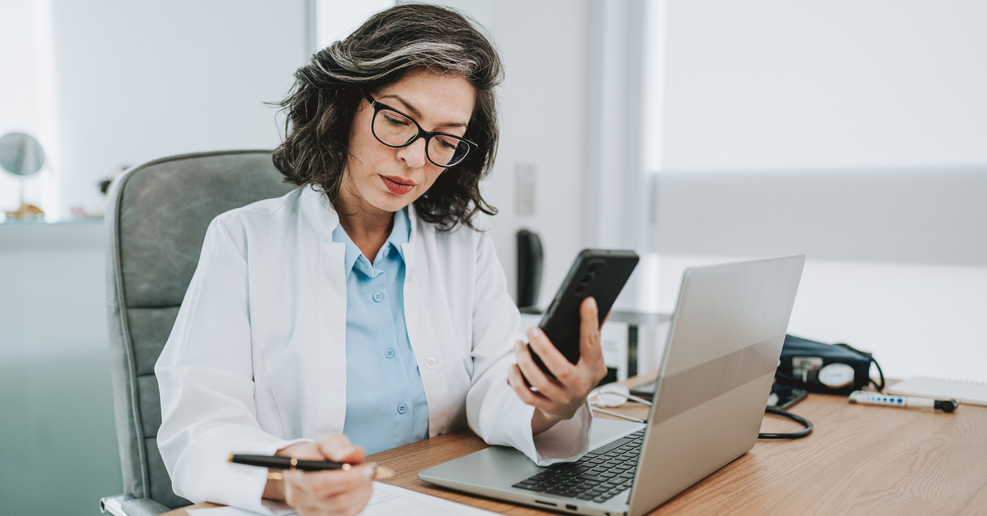 doctor sitting at desk looking at computer and phone