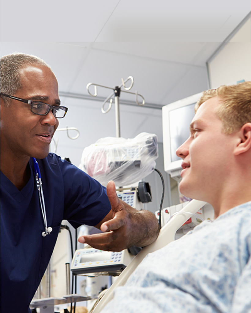 Doctor speaking with a patient in a hospital bed as part of patient-centered emergency medicine solutions.