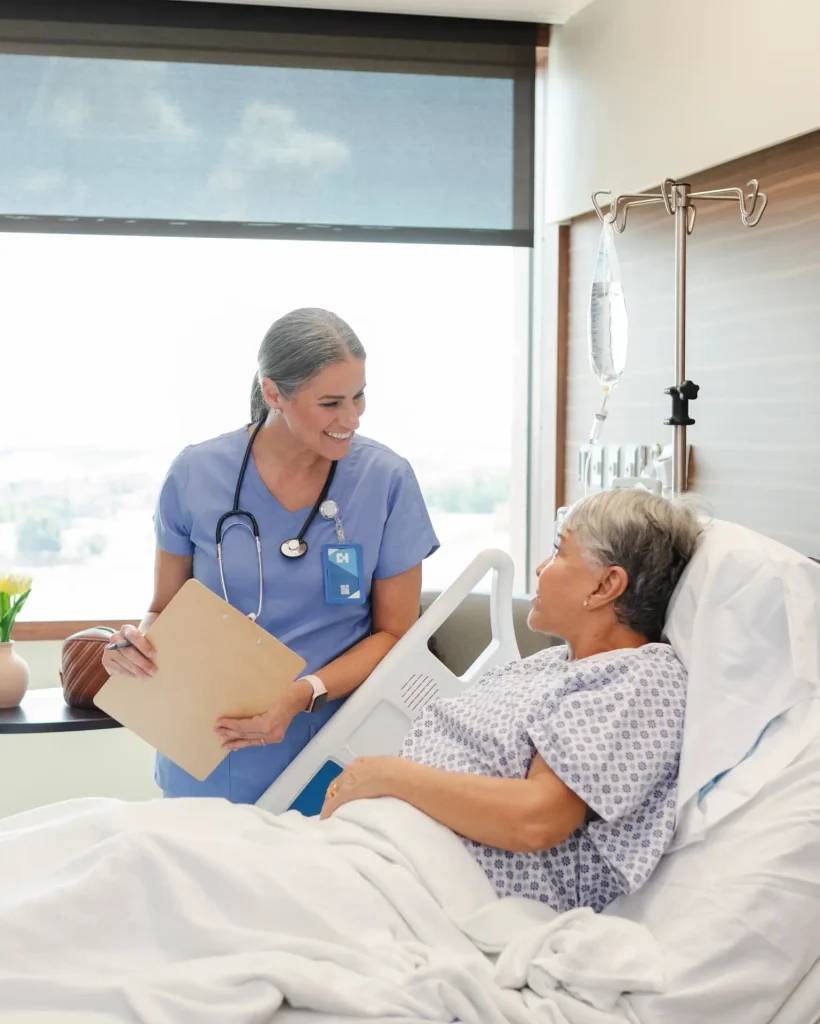 Nurse smiling at a patient in a hospital bed, reflecting compassionate hospital medicine services.