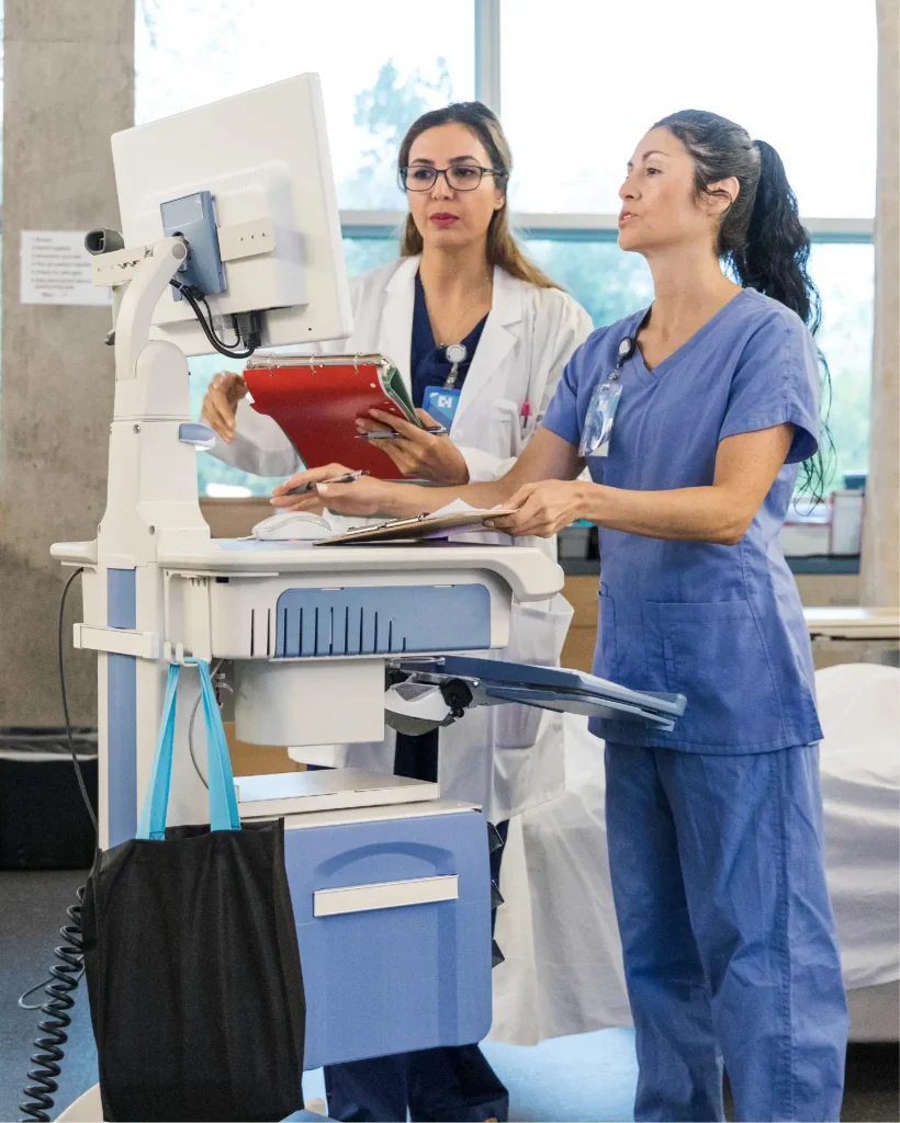 Doctor and nurse discussing an emergency room patient at a medical cart, demonstrating clinical healthcare core capabilities.
